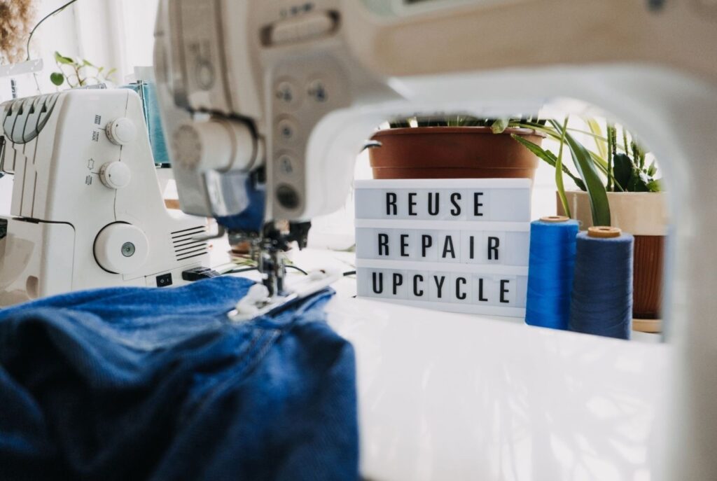 Machine à coudre et matériaux de surcyclage dans un studio de design de mode avec panneau "réutiliser réparer recycler" designers de mode surcyclant de manière durable et circulaire créative