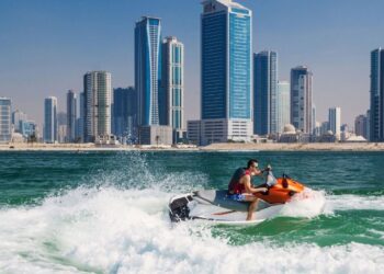 人们在迪拜JBR海滩享受水上摩托和沙滩运动，以码头天际线为背景，展示了阿拉伯湾海岸线上热门的水上活动，带来肾上腺素飙升的刺激和迷人的景色