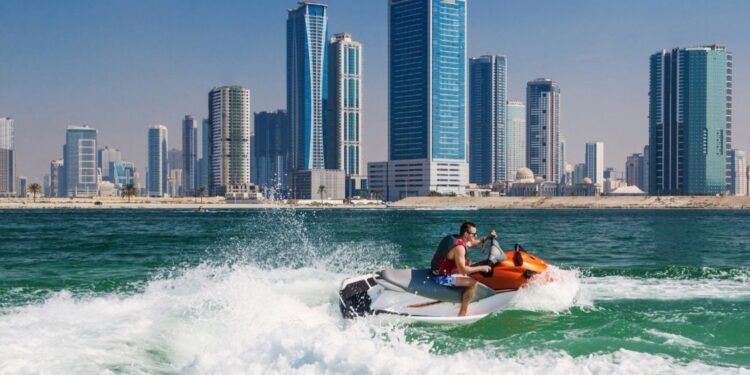 人们在迪拜JBR海滩享受水上摩托和沙滩运动，以码头天际线为背景，展示了阿拉伯湾海岸线上热门的水上活动，带来肾上腺素飙升的刺激和迷人的景色