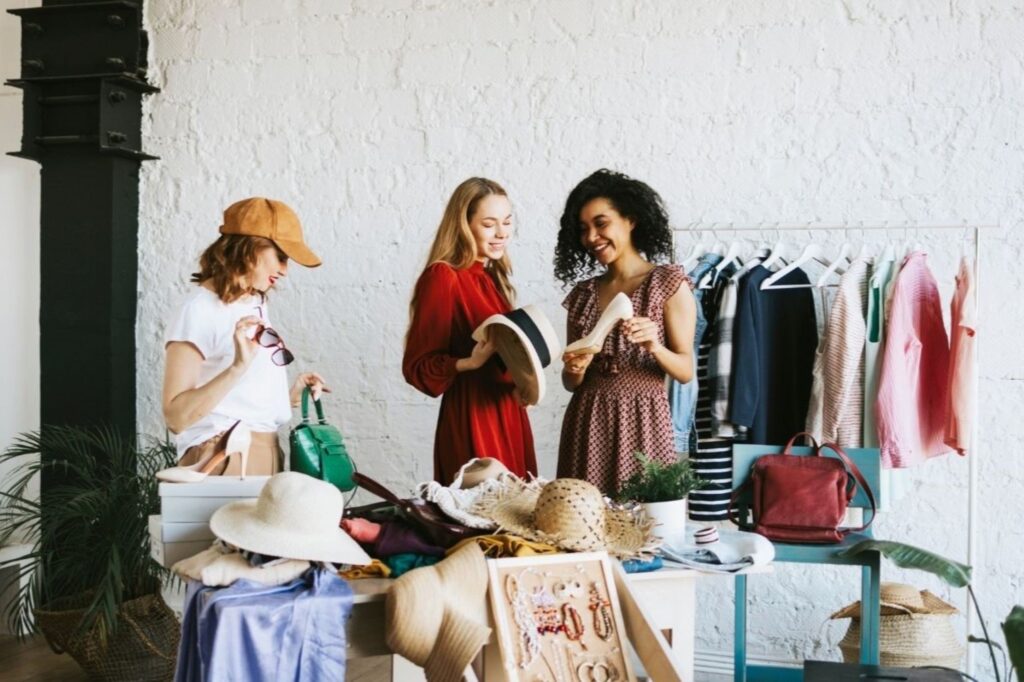 दुबई में इको-फ्रेंडली फैशन बुटीक में सस्टेनेबल पार्टी वियर ब्राउज़ करती महिलाएं, ऑर्गेनिक फैब्रिक और कारीगर-निर्मित उत्सव के कपड़ों के साथ नैतिक खरीदारी के अनुभव का प्रदर्शन करती हैं