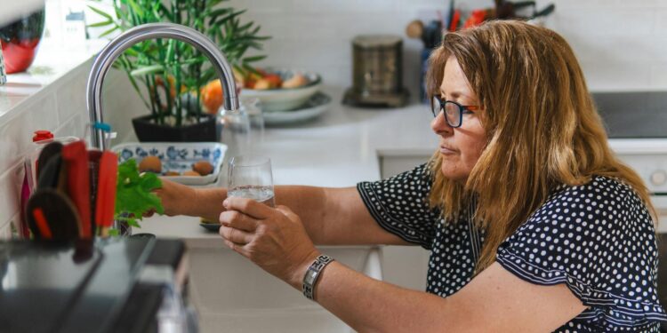 woman-checking-kitchen-faucet-pexels - DUBAIwebzine Une femme inspectant un robinet de cuisine dans une maison moderne de Dubaï pour réduire la consommation d'eau domestique