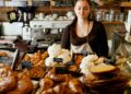 A smiling woman selecting a treat at one of Dubai's gluten-free bakeries, surrounded by fresh baked goods on a cafe counter.
