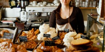 A smiling woman selecting a treat at one of Dubai's gluten-free bakeries, surrounded by fresh baked goods on a cafe counter.