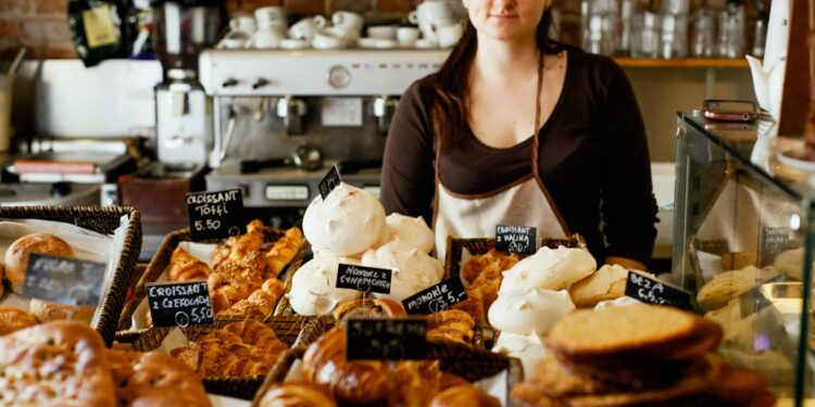 A smiling woman selecting a treat at one of Dubai's gluten-free bakeries, surrounded by fresh baked goods on a cafe counter.