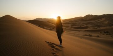 woman-watching-desert-sunrise-dunes-unsplash - DUBAIwebzine 一位旅客在迪拜附近夏季沙漠逃离期间观看金色沙丘上的日出