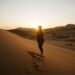 امرأة تراقب شروق الشمس في الصحراء من فوق الكثبان - DUBAIwebzine مسافر يراقب شروق الشمس فوق الكثبان الذهبية أثناء هروب صحراوي صيفي بالقرب من دبي