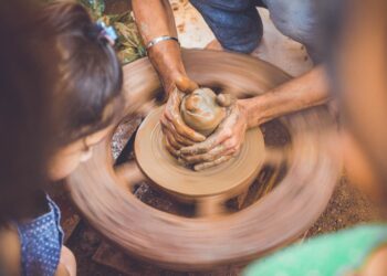 A young child learning to shape clay at a pottery wheel during creative workshops in Dubai, guided by an instructor.