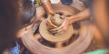 A young child learning to shape clay at a pottery wheel during creative workshops in Dubai, guided by an instructor.