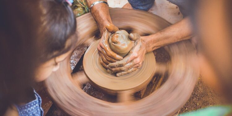 child-doing-pottery-unsplash - DUBAIwebzine A young child learning to shape clay at a pottery wheel during creative workshops in Dubai, guided by an instructor.