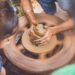 child-doing-pottery-unsplash - DUBAIwebzine A young child learning to shape clay at a pottery wheel during creative workshops in Dubai, guided by an instructor.