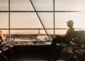 A traveler at Dubai International Airport checking long-haul fares on a smartphone before booking a summer flight