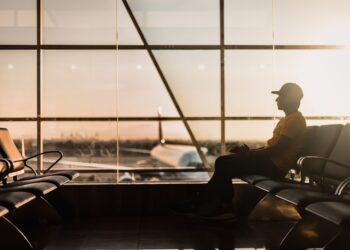 A traveler at Dubai International Airport checking long-haul fares on a smartphone before booking a summer flight