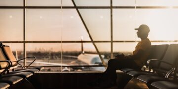 A traveler at Dubai International Airport checking long-haul fares on a smartphone before booking a summer flight