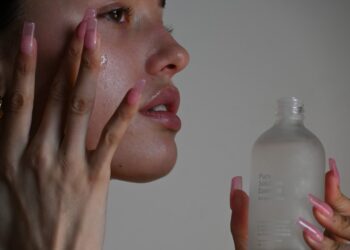 A woman applying Dubai skincare cream in a bright modern bathroom, looking into a mirror with a calm expression
