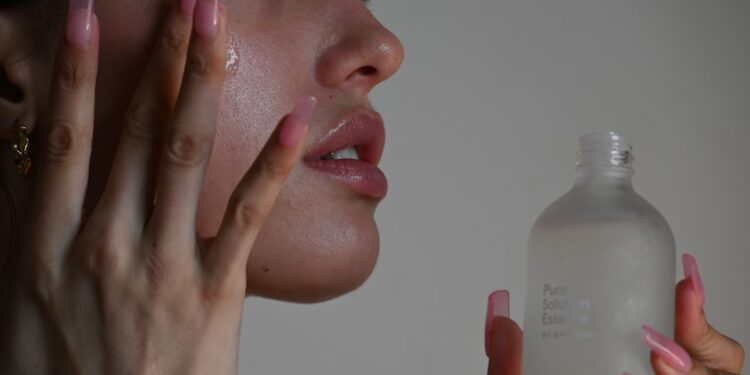 woman-applying-face-cream-unsplash - DUBAIwebzine A woman applying Dubai skincare cream in a bright modern bathroom, looking into a mirror with a calm expression