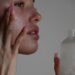 woman-applying-face-cream-unsplash - DUBAIwebzine A woman applying Dubai skincare cream in a bright modern bathroom, looking into a mirror with a calm expression