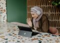 woman-laptop-working-in-a-cafe-dubai-coworking-unsplash - DUBAIwebzine A digital nomad working at a bright coworking space in Dubai, with a laptop open and city views behind her