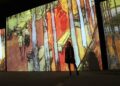 A woman walks through a glowing digital projection room at an immersive art experience inside a Dubai mall