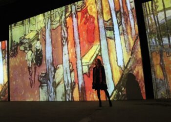 A woman walks through a glowing digital projection room at an immersive art experience inside a Dubai mall