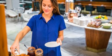 A woman carefully reading allergen labels at a gluten-free buffet spread in a Dubai hotel restaurant