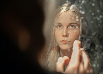 woman-applying-moisturizer-mirror-unsplash - DUBAIwebzine A woman applying a rich moisturizer as part of her updated skincare regimen during Dubai's seasonal humidity drop