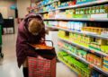 woman-shopping-bag-supermarket-unsplash - DUBAIwebzine A woman choosing loose produce at a Dubai supermarket, reducing plastic use with a reusable mesh shopping bag