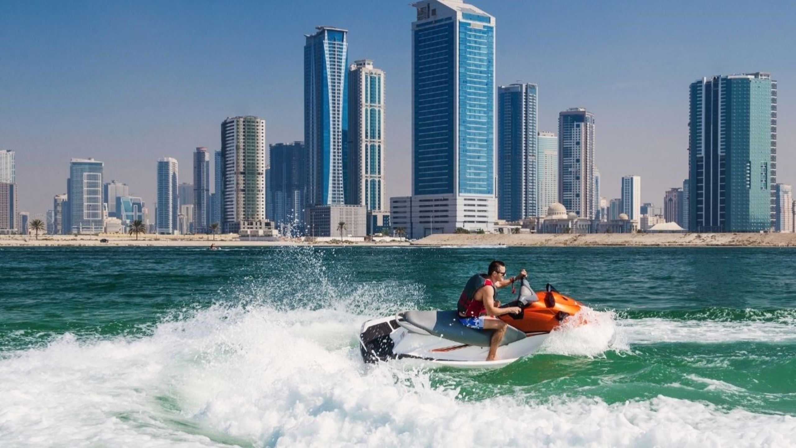 Pessoas a aproveitar desportos de praia e jet ski em JBR Dubai com o skyline da Marina ao fundo, destacando atividades aquáticas populares ao longo da costa do Golfo Pérsico, que oferecem adrenalina e vistas panorâmicas