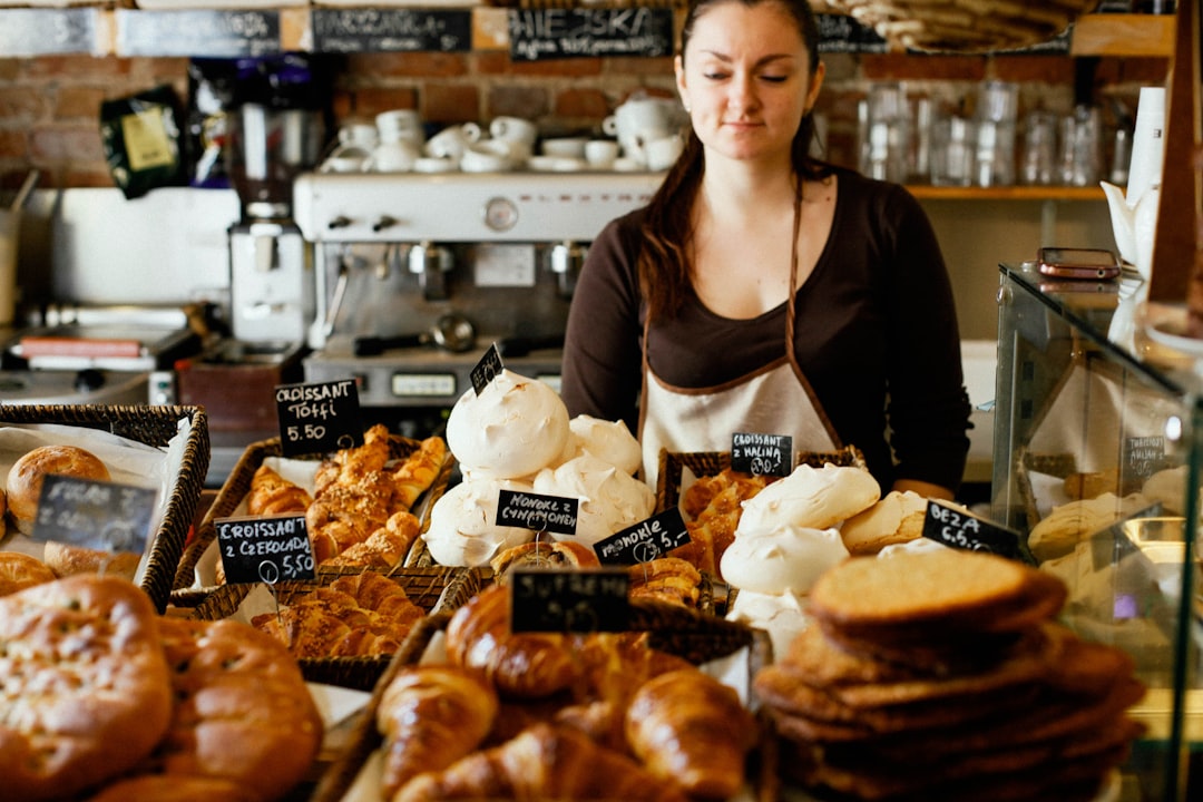 Une femme souriante sélectionnant une gourmandise dans l'une des boulangeries sans gluten de Dubaï, entourée de produits frais sortis du four sur le comptoir d'un café.